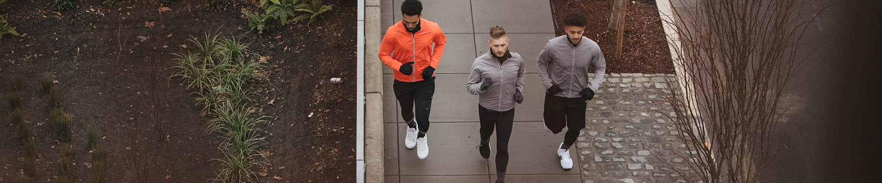 An aerial view of three men wearing Showers Pass winter running gear, jogging side by side on a city sidewalk.