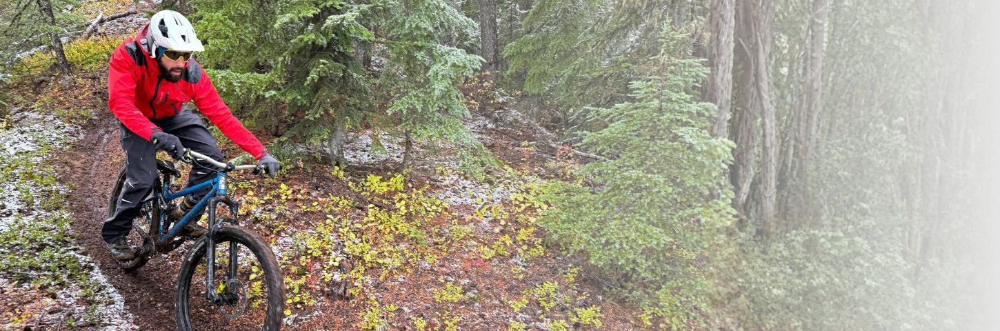 Person mountain biking on a trail in a forest during a snowstorm