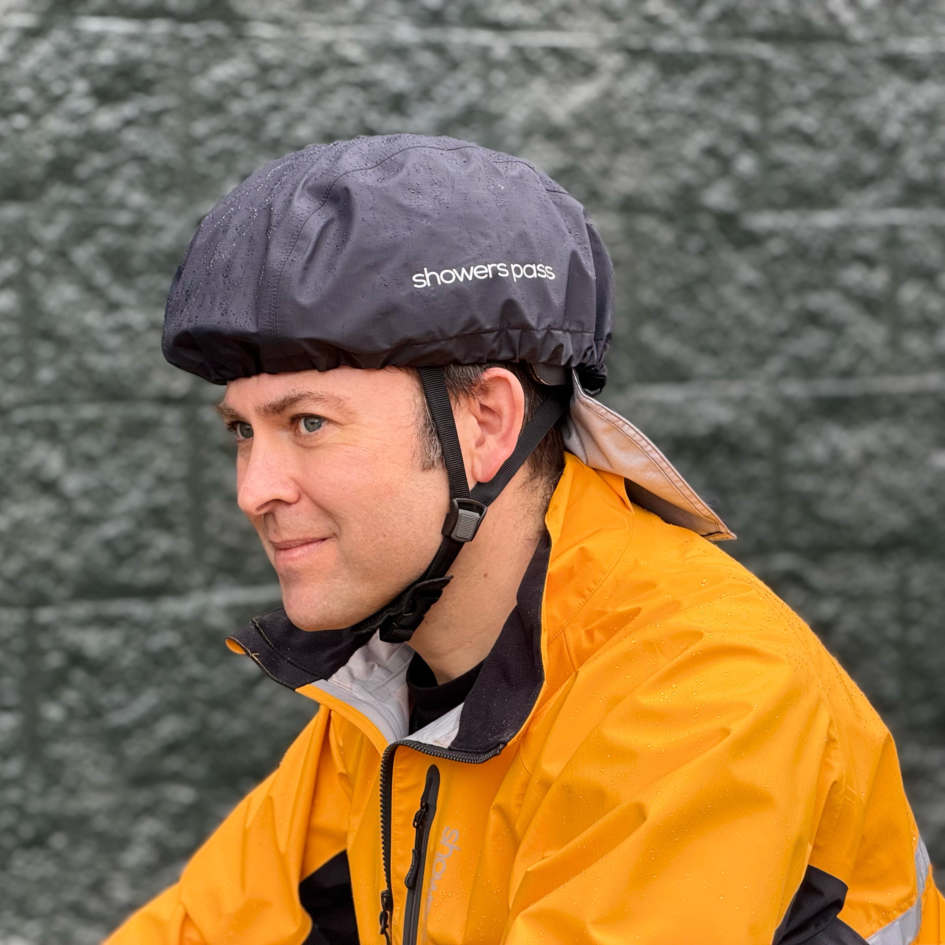 Person wearing a yellow raincoat and black helmet Cover with Showers Pass branding