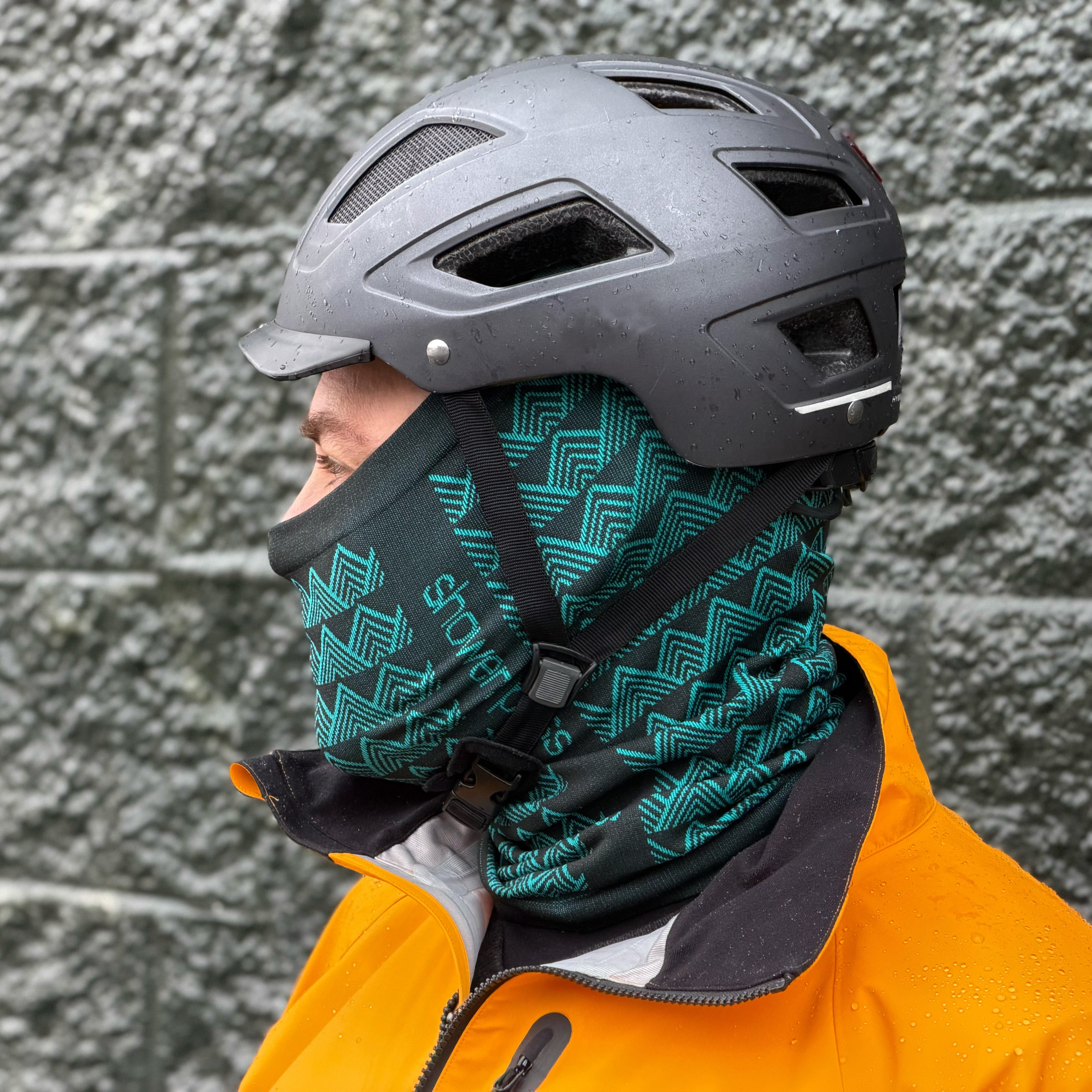 Person wearing a helmet and an orange jacket with a patterned neck gaiter